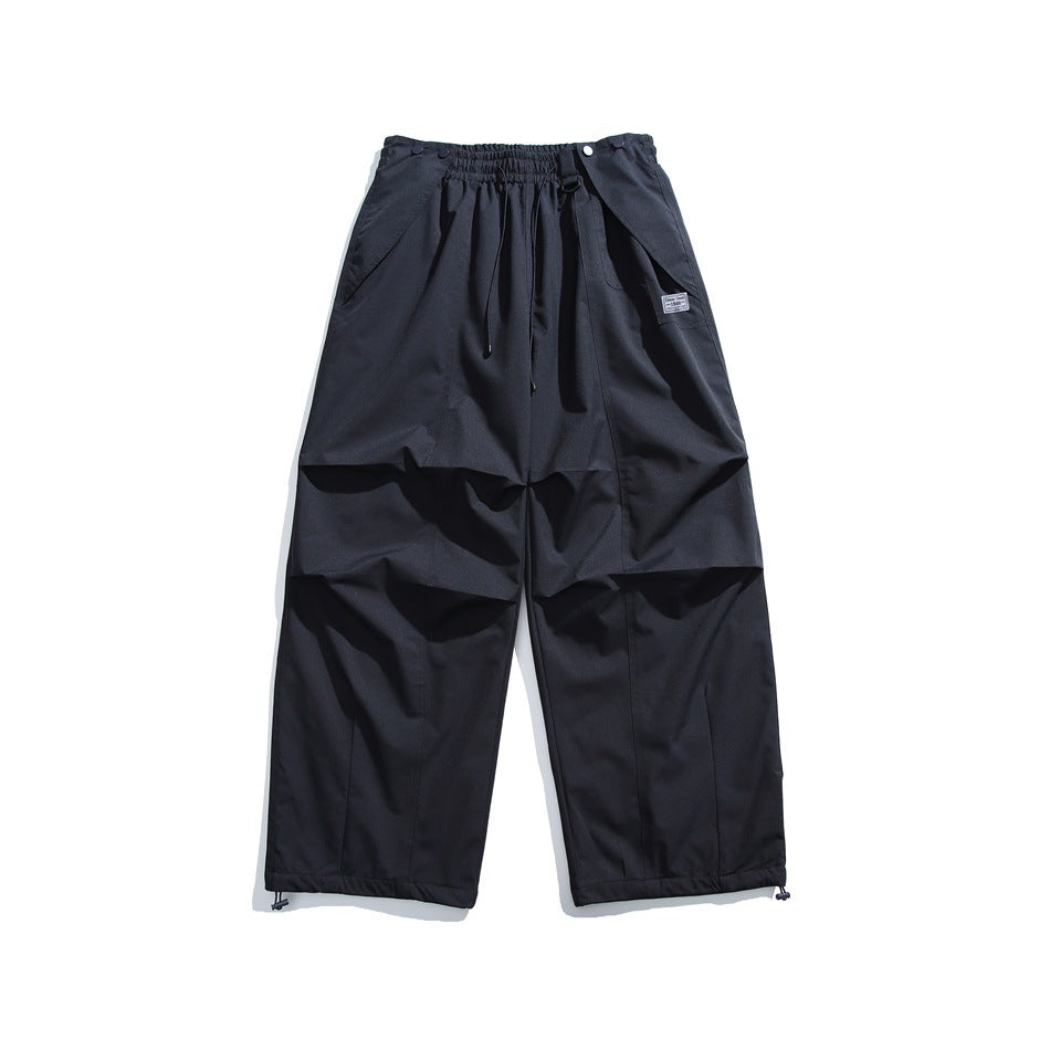 Dark black-blue wide-leg drawstring pants laid flat, with knee pleats, thigh patch and drawcord hems