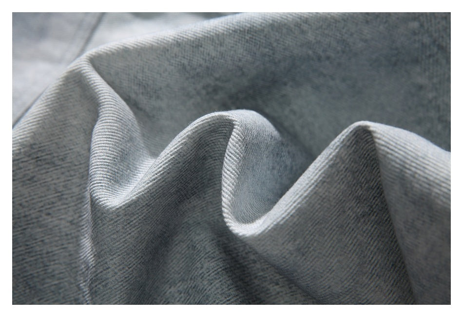 Close-up of light gray denim fabric draped into soft folds, showing its diagonal weave.
