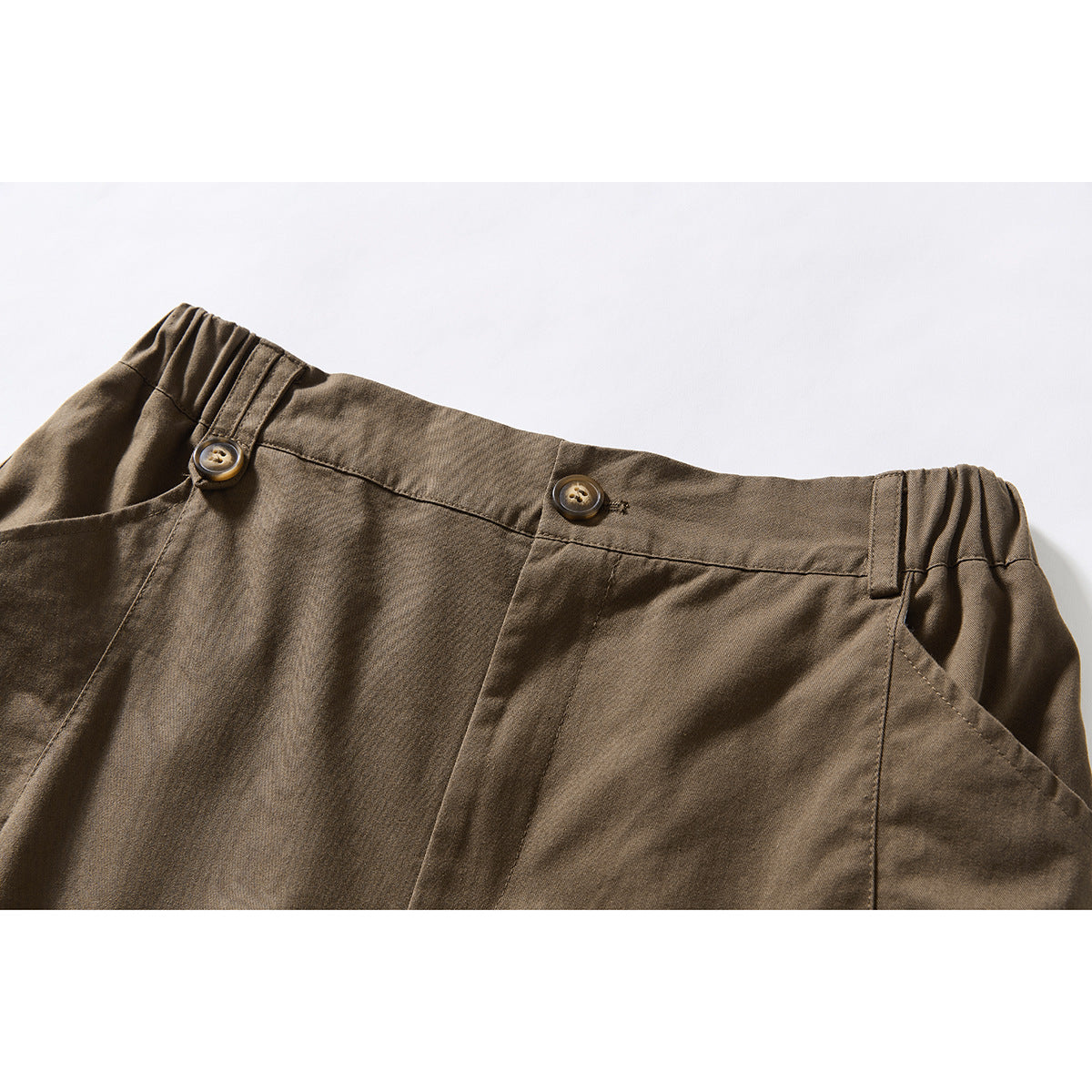 Close-up of brown shorts showing the buttoned waistband, side elastic, belt loops, and angled front pocket.
