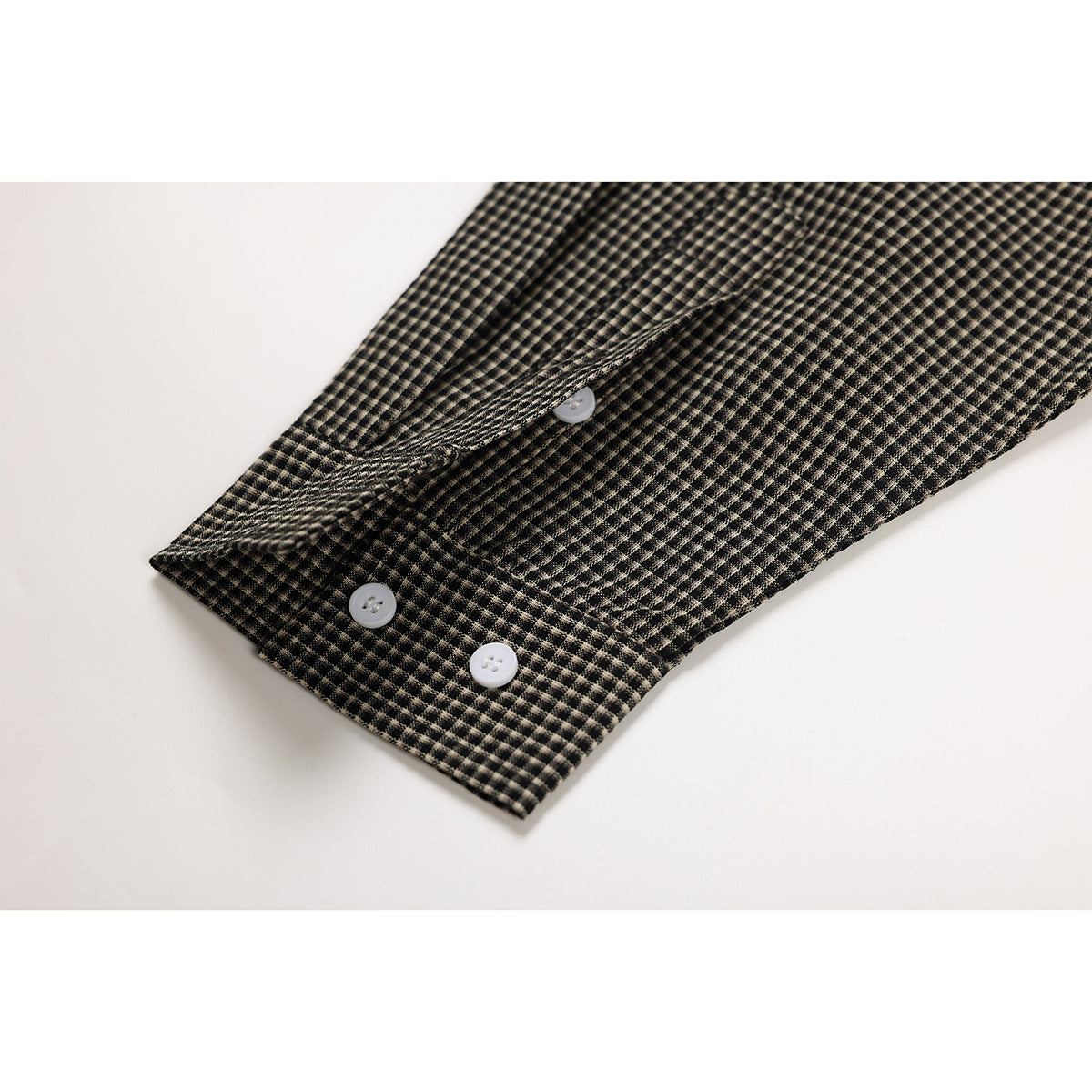 Close-up of a buttoned cuff on a black and beige micro-check shirt.