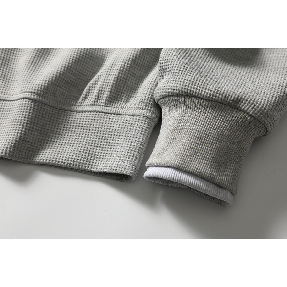 Close-up of a light gray jacket's ribbed cuff and hem, with a white layer visible underneath.