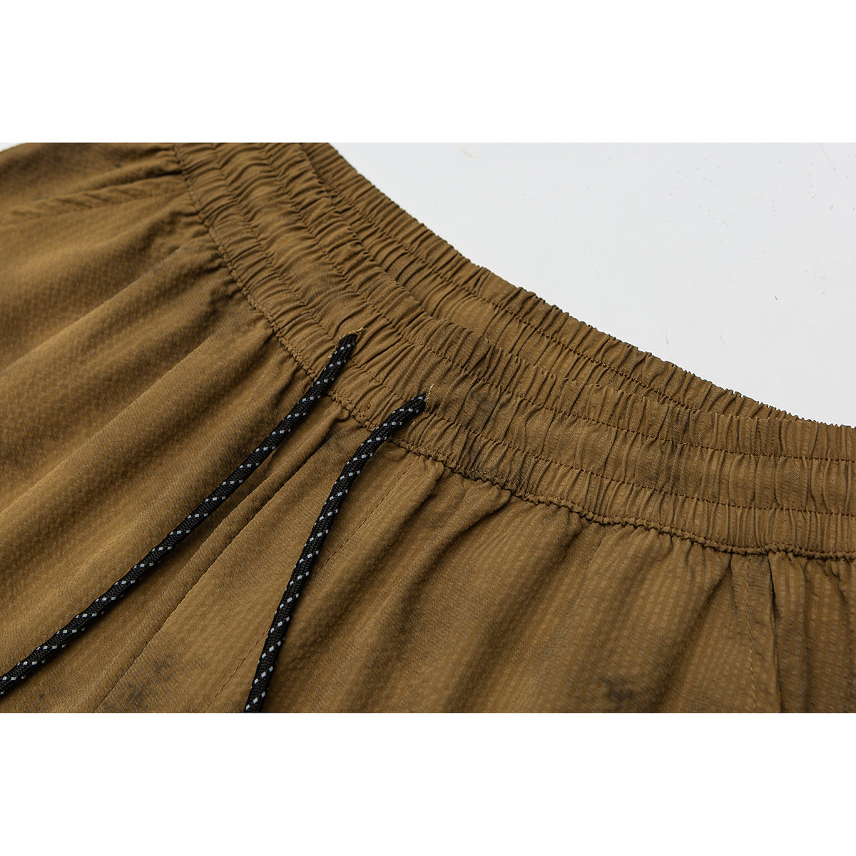 Close-up of ochre-brown shorts showing the gathered elastic waistband and black drawcords with white flecks.
