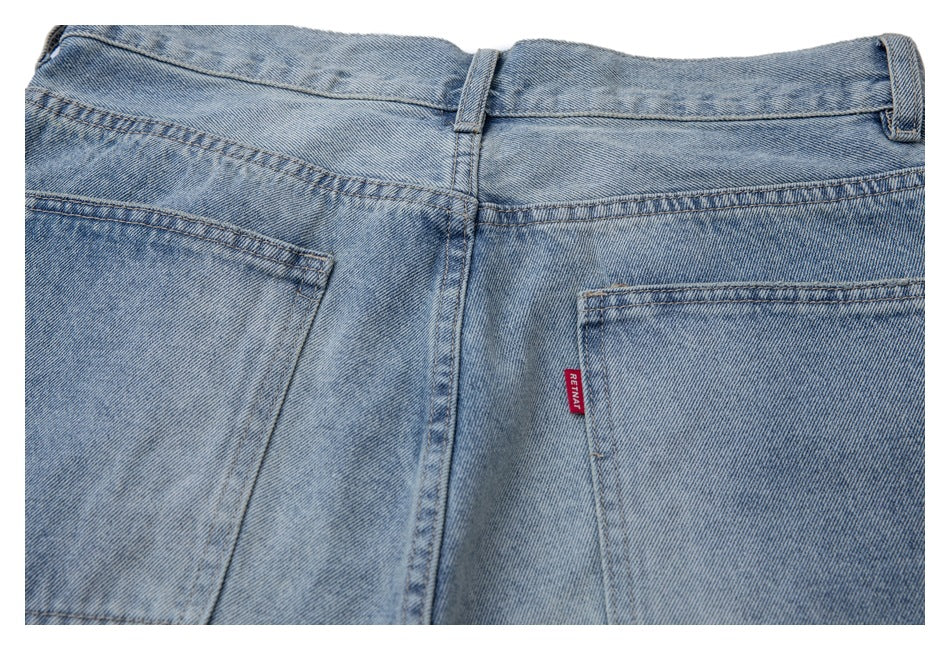 Close-up of the back waistband and two pockets on light blue washed jeans, with a small red tab.