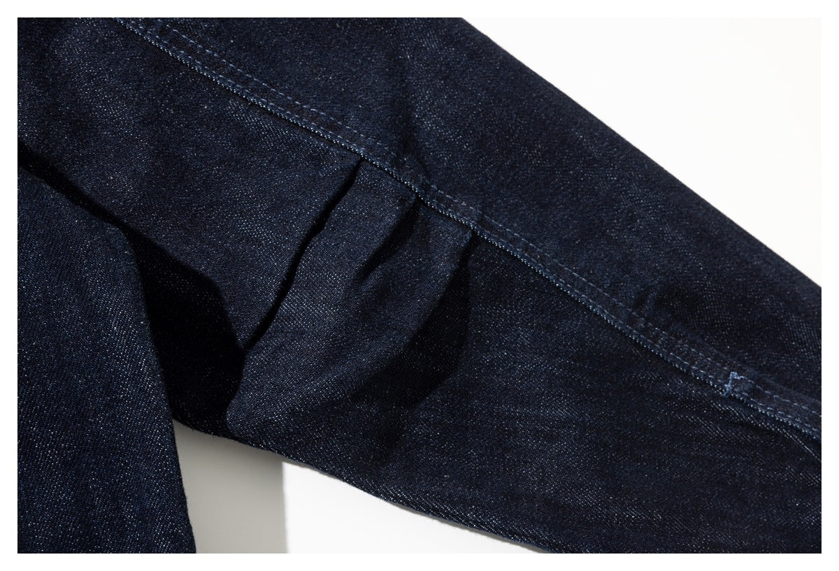 Close-up of dark indigo denim jacket sleeve and underarm seams with visible stitching and a folded pleat.