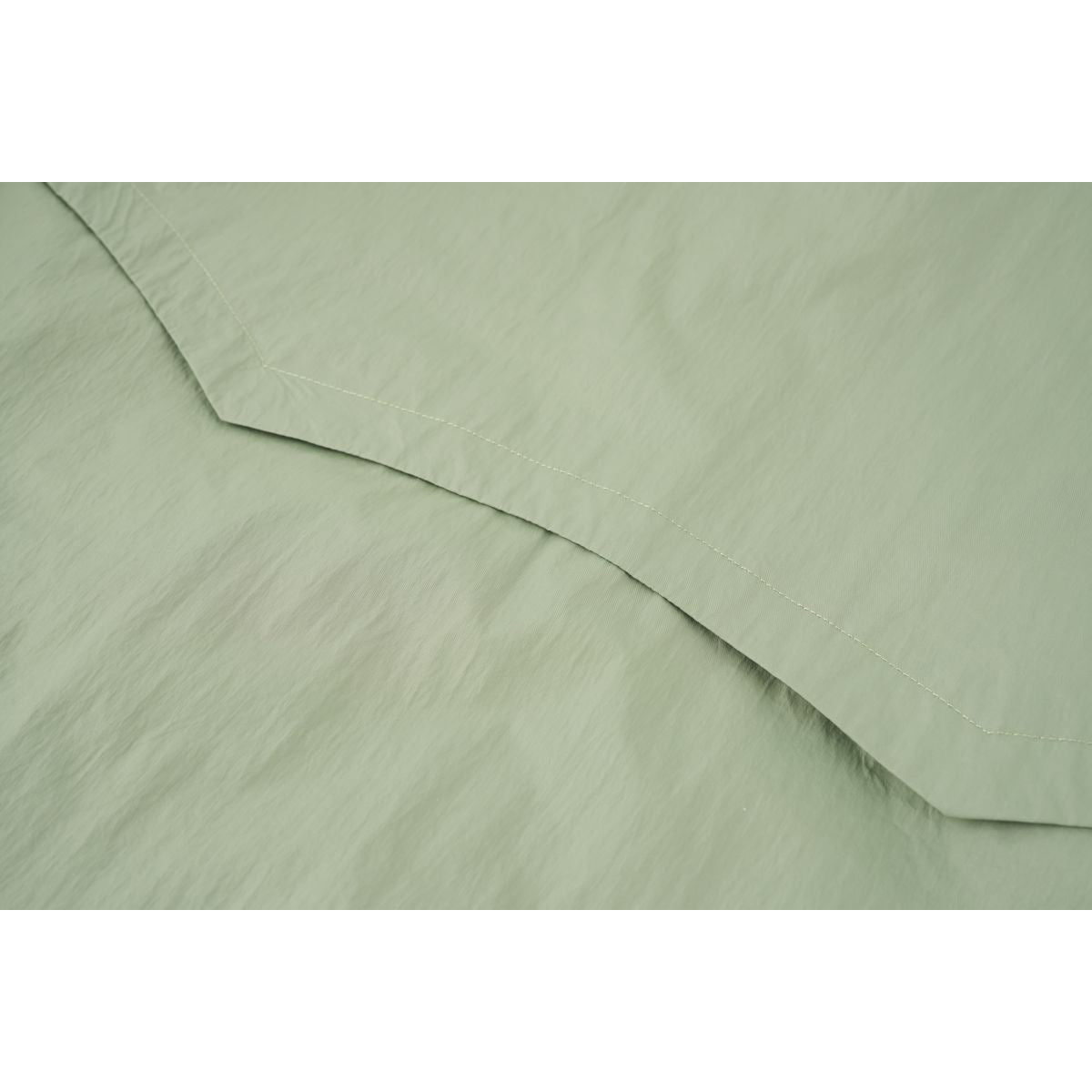Close-up of a pale sage-green jacket panel showing a curved stitched seam.