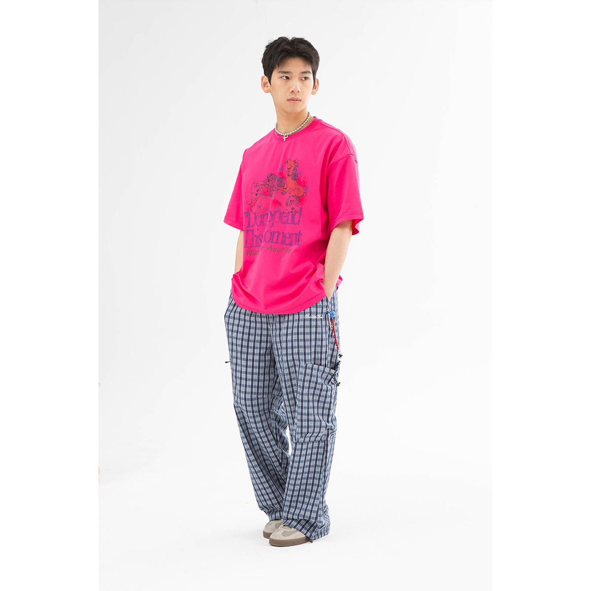 Model wearing a bright pink graphic T-shirt and loose blue-gray plaid trousers.