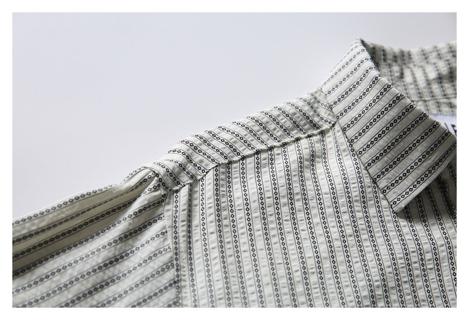 Close-up of the pointed collar and shoulder seam on the cream shirt with black patterned stripes.