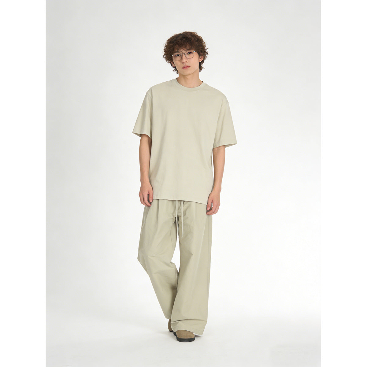 Model wearing a pale sage oversized T-shirt and matching loose drawstring trousers against a plain studio background.