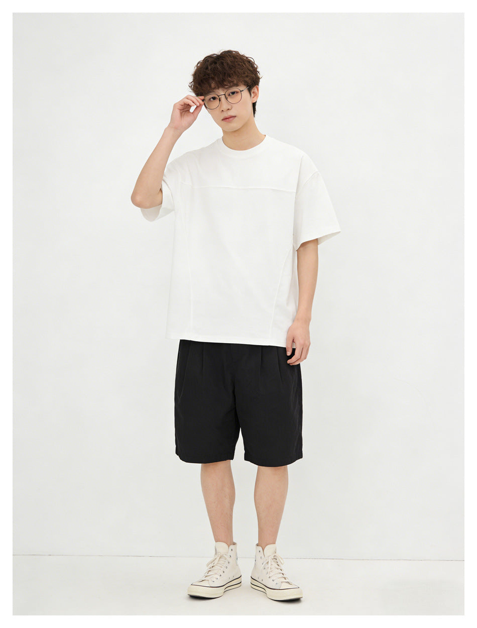 Model wearing a white oversized short-sleeve crew-neck T-shirt with a horizontal chest seam and black shorts.