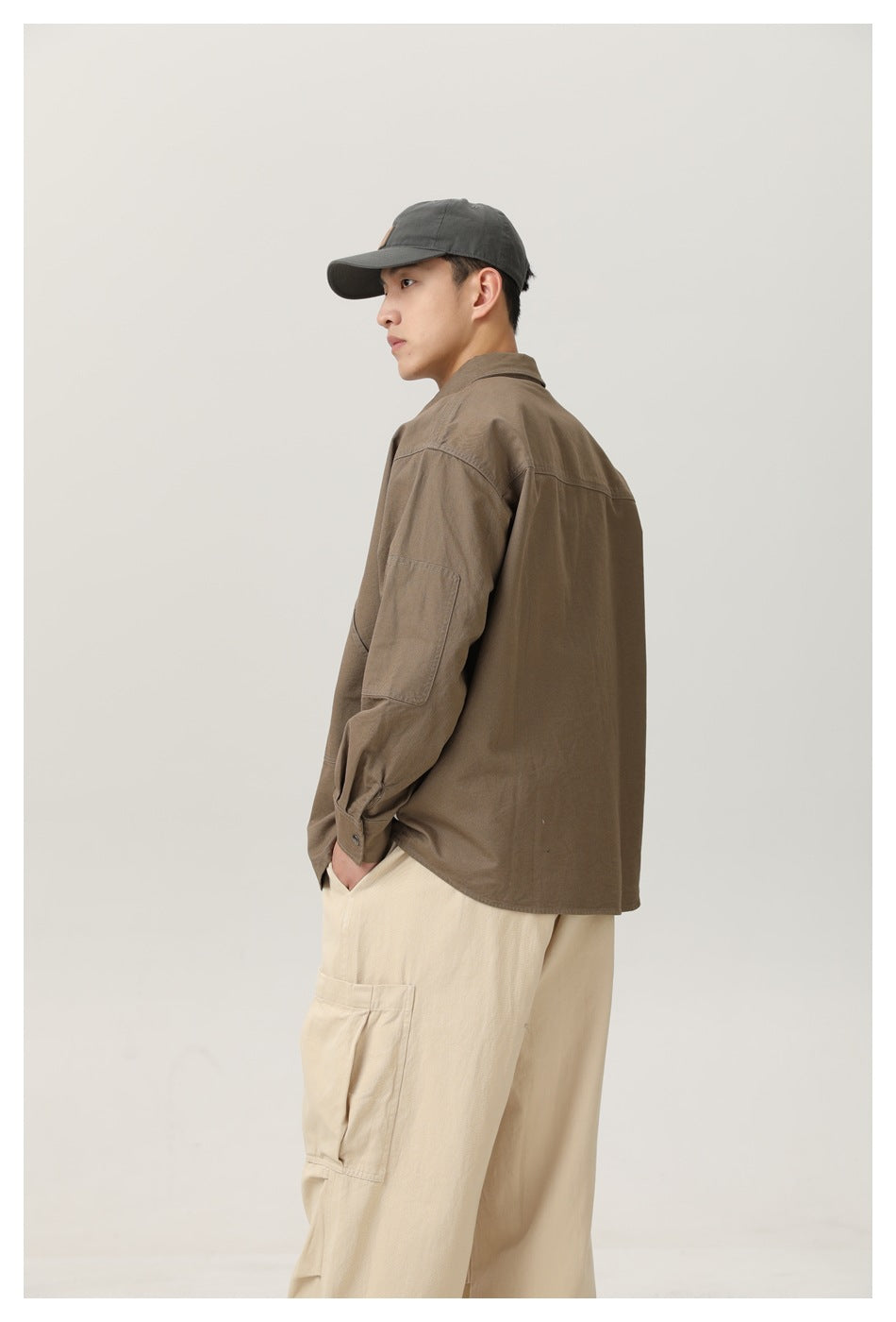 Side view of a man in an olive-brown shirt showing the sleeve patch panel, with hands in beige cargo pants pockets