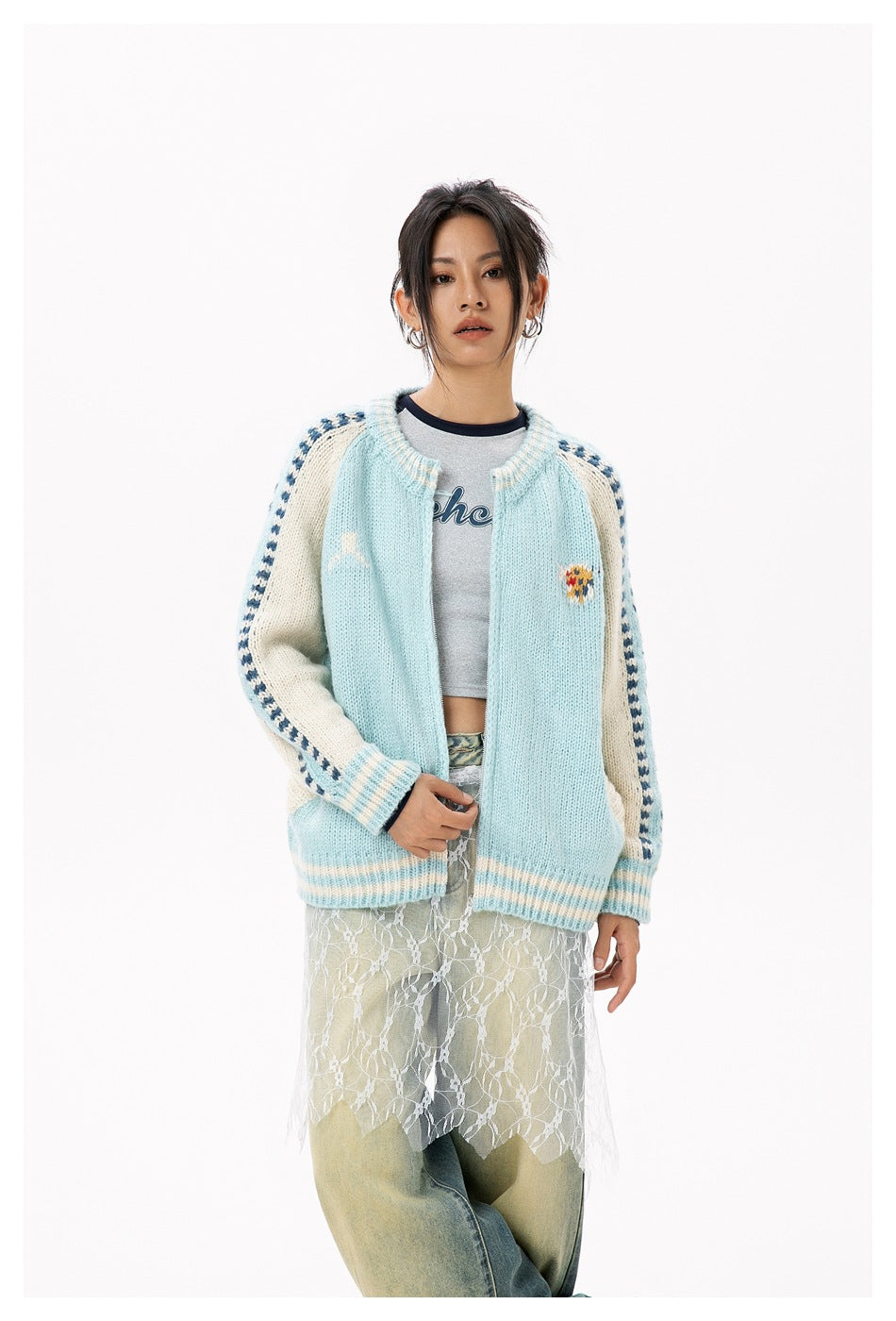 Model wearing an open pale blue cardigan with cream sleeves, blue patterned stripes and a small colorful chest motif.
