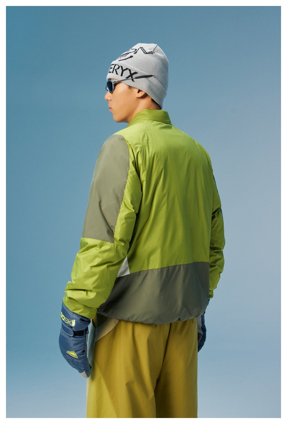 Close rear three-quarter view of a lime green jacket with gray sleeve and hem panels and a white side insert.