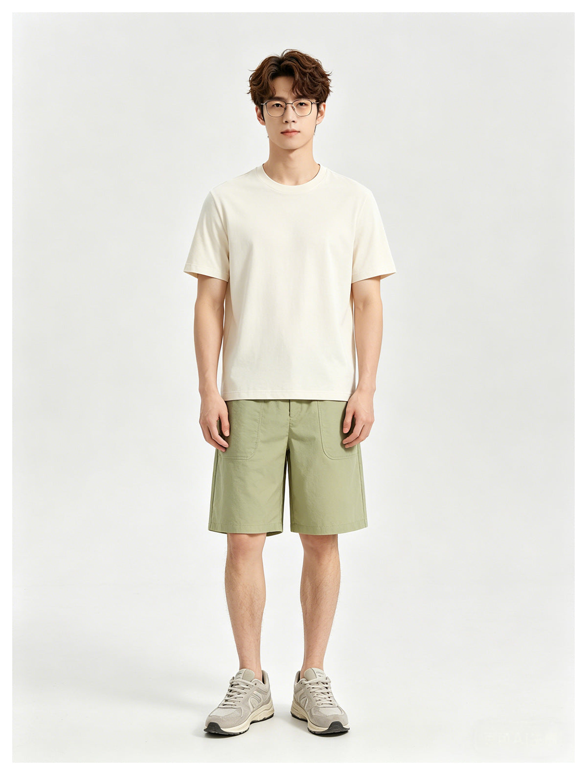 Model wearing an ivory crew-neck T-shirt with light olive shorts and gray sneakers.