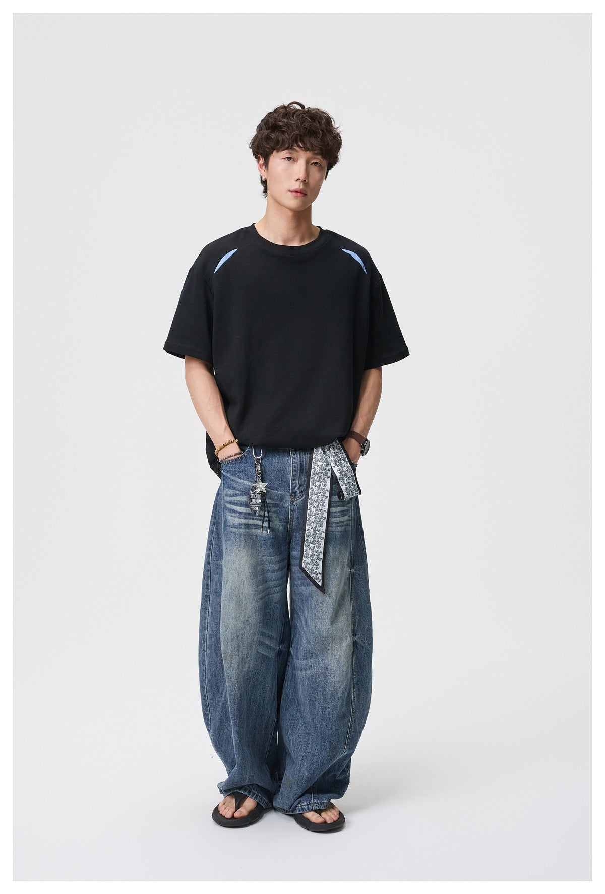 Model wearing a black relaxed crewneck T-shirt with light-blue shoulder accents and wide-leg jeans, front view