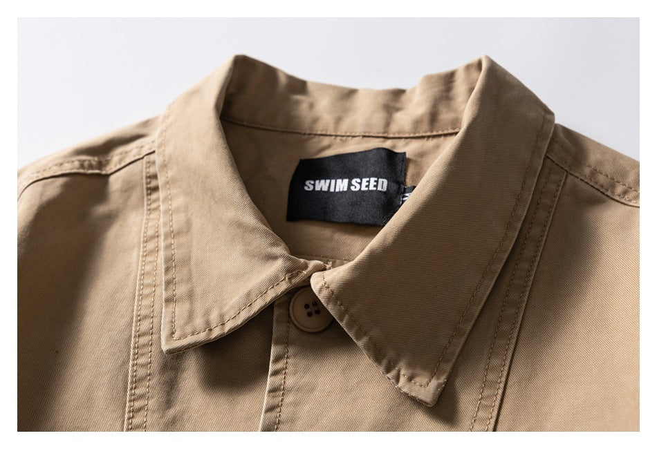 Close-up of the tan jacket's pointed collar, top button, stitching, and black neck label.