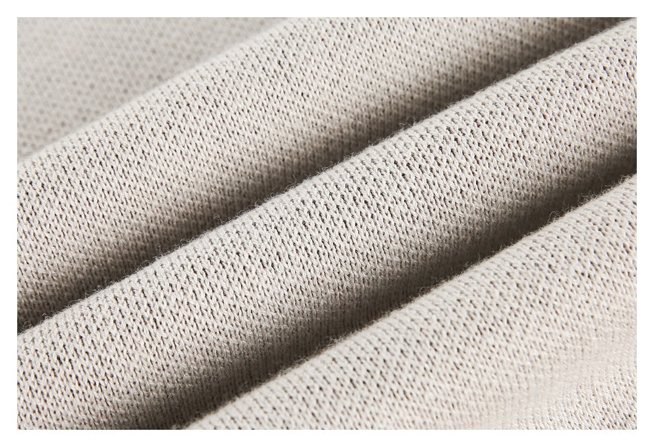 Close-up of light beige knit fabric arranged in soft folds, showing its stitch texture.