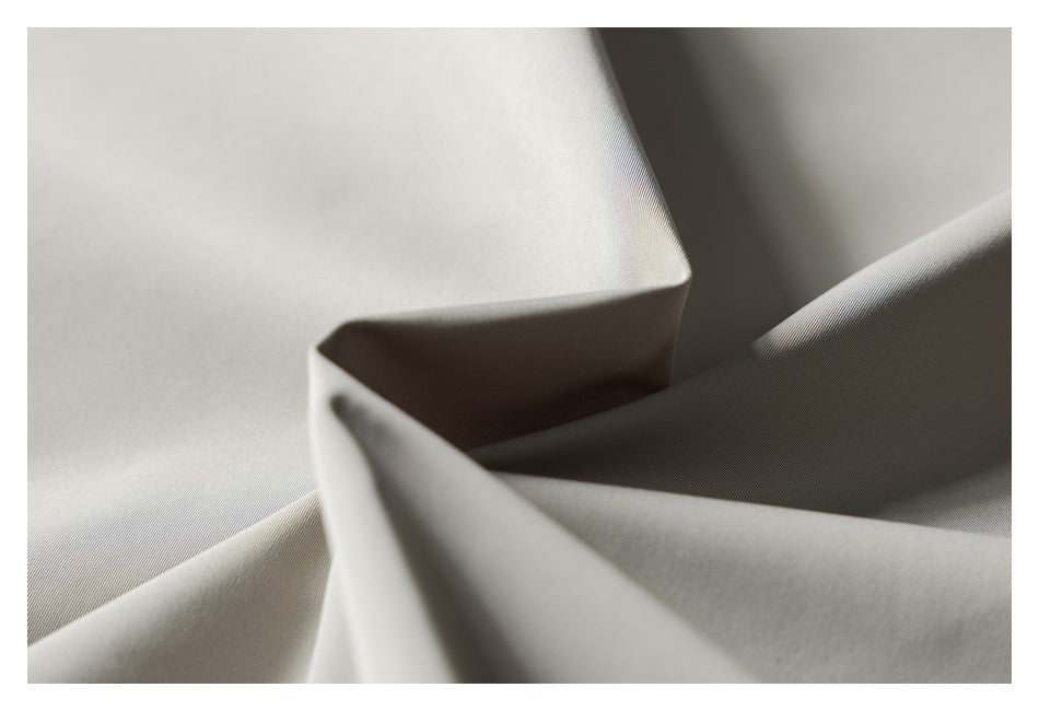 Close-up of smooth light gray fabric folded into soft, angular drapes.