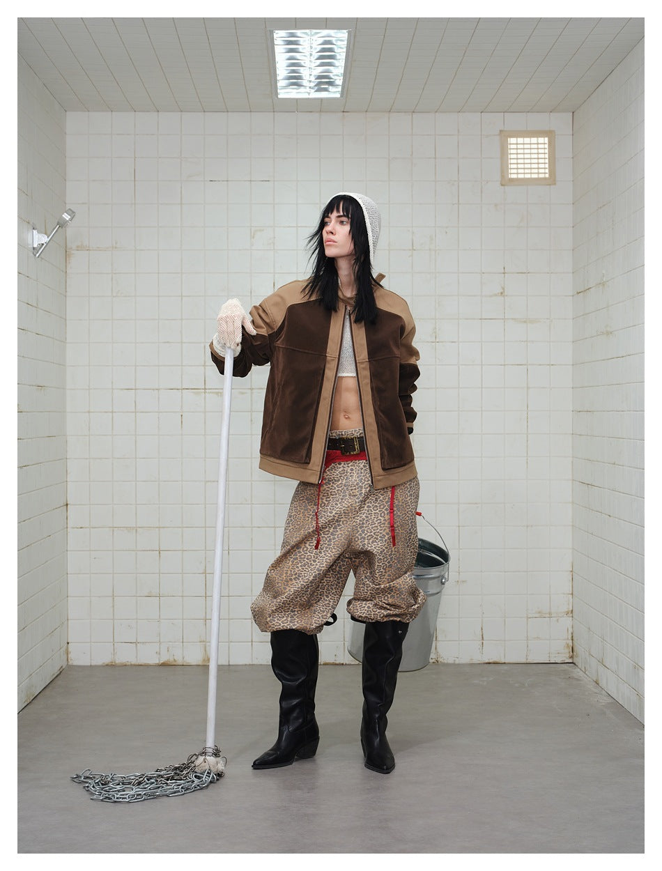 Model wearing a two-tone brown zip jacket, leopard-print trousers and black boots, holding a mop.