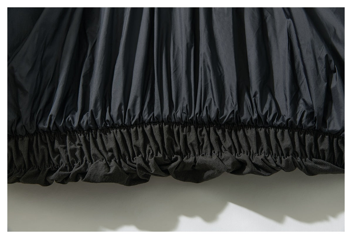Close-up of a dark garment's gathered elastic hem, with shiny fabric above a textured lower panel.
