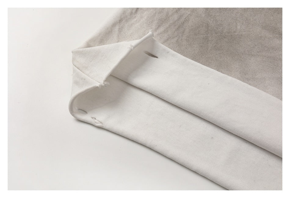 Close-up of an off-white garment edge with small openings and stitching, beside gray fabric.