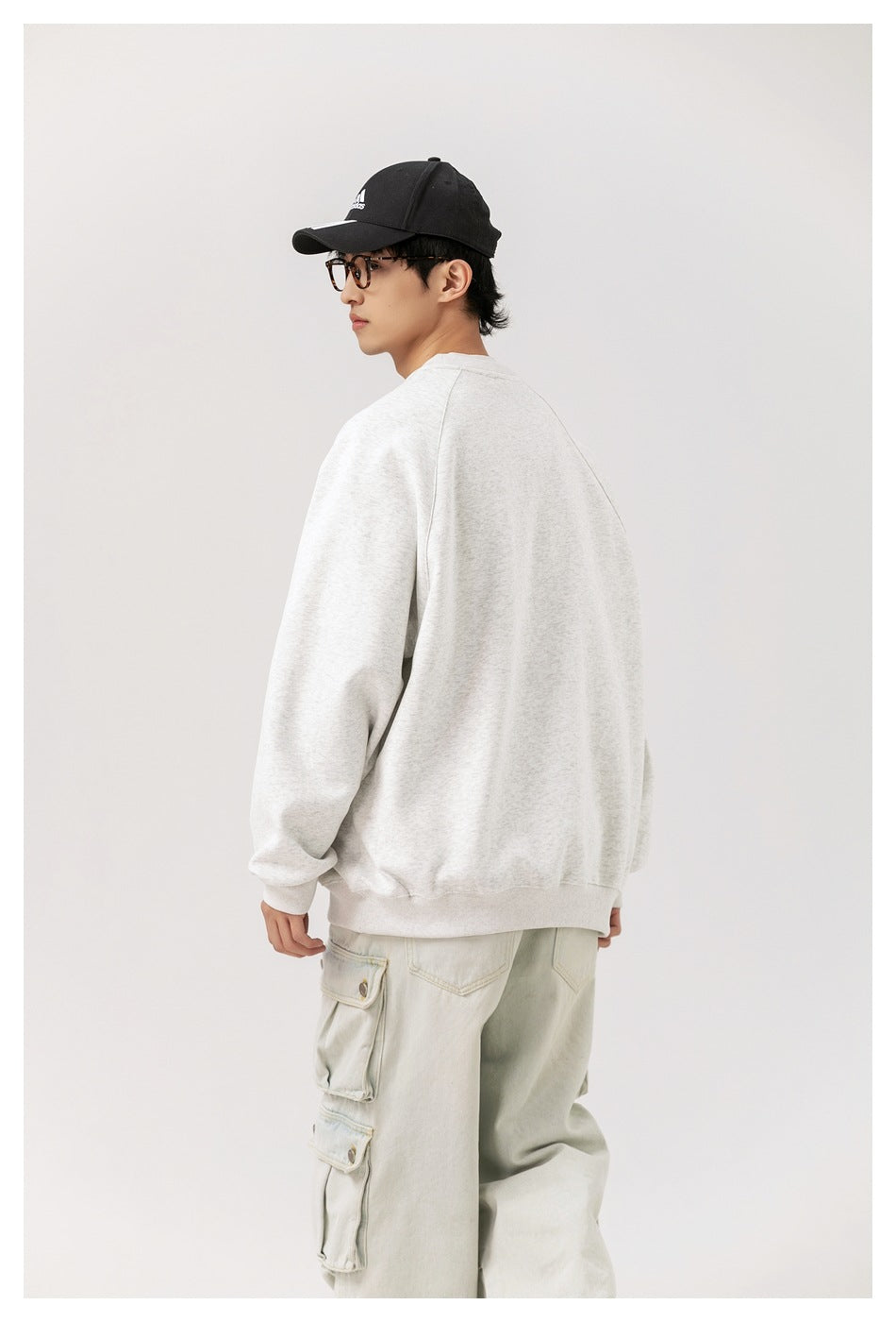 Model turned away, showing the back and side of a plain light gray sweatshirt.