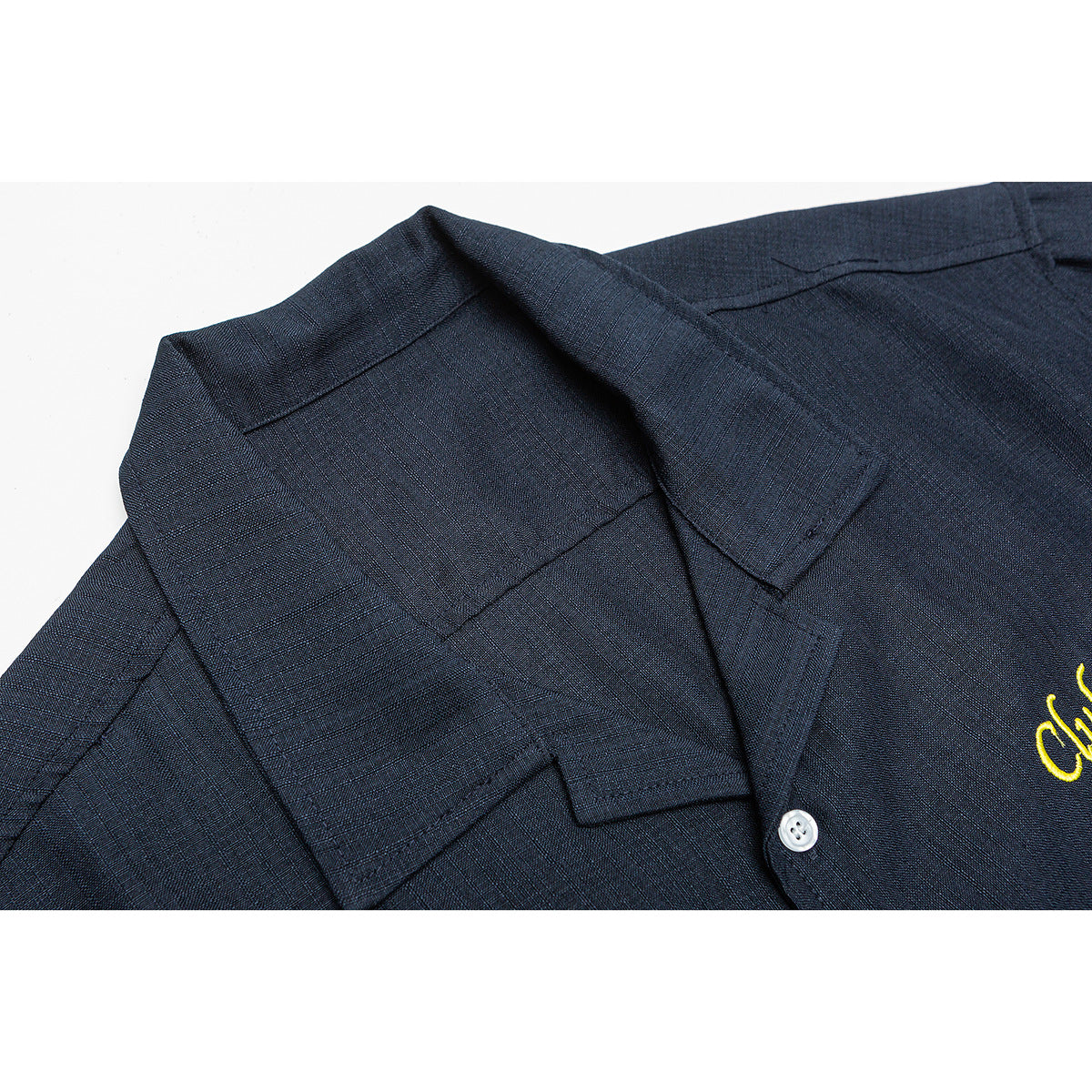 Close-up of a dark navy short-sleeve shirt collar and button placket, with a glimpse of yellow embroidery.