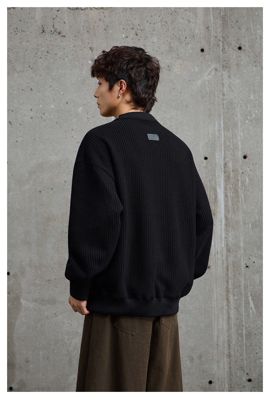 Model showing the back of an oversized black textured crewneck sweatshirt with a small label below the collar.