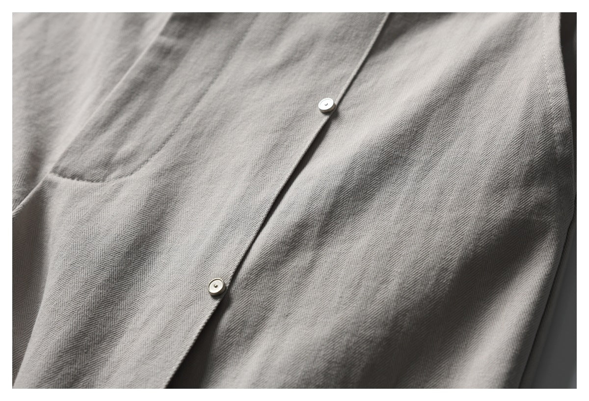 Close-up of gray herringbone trousers with a diagonal placket and two small metal fasteners.