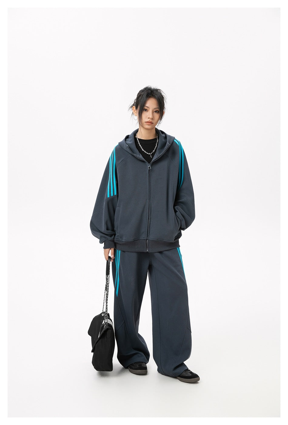 Model wearing a charcoal zip-up hoodie and wide-leg pants with bright cyan stripes, shown full length.