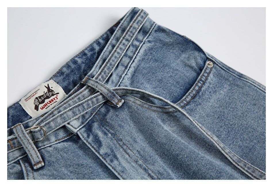 Close-up of the upper front of blue jeans showing the waistband, belt loops, button, front pocket, and sewn-in label.