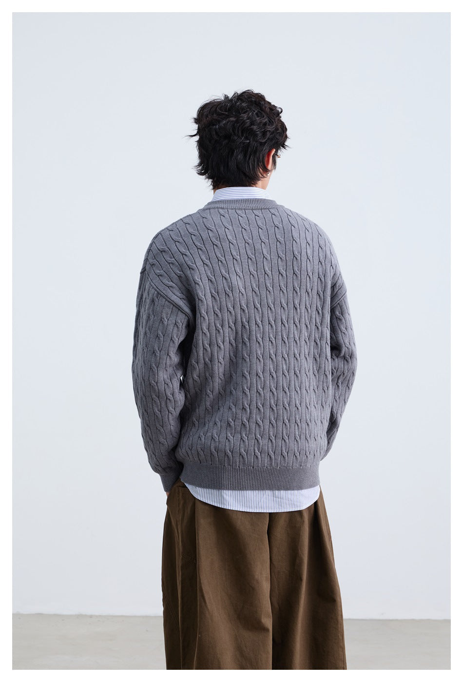 Back view of model wearing gray cable-knit sweater over a striped shirt with brown wide-leg pants