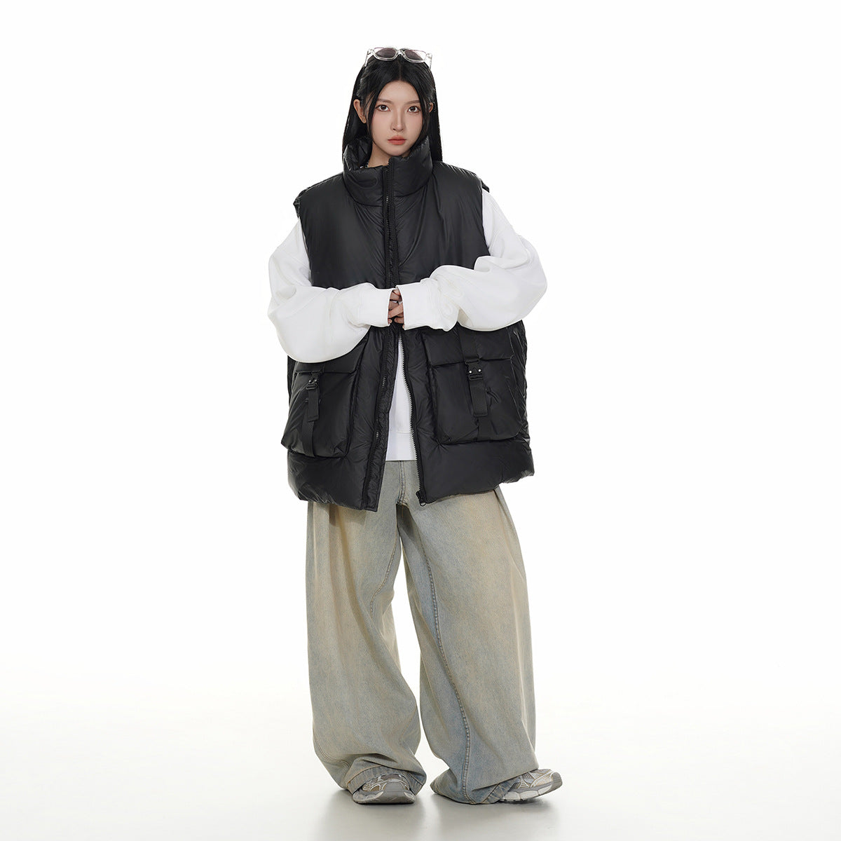 Full-length view of a model wearing a black padded zip vest with large buckle-detail pockets over a white top.