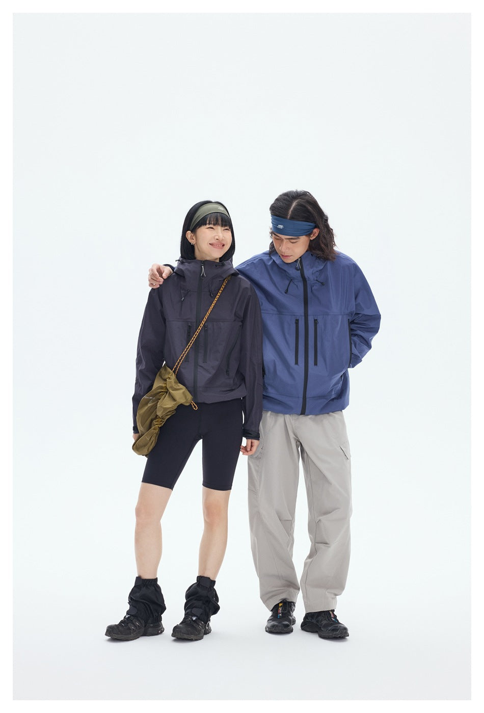 Two models pose together in charcoal and blue hooded jackets, with shorts and light gray cargo pants.