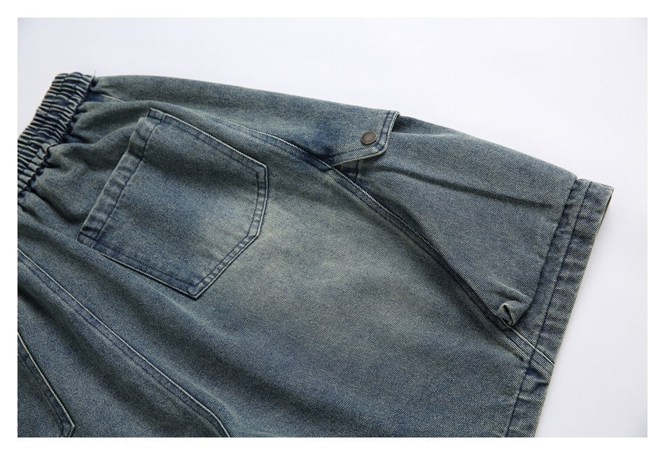 Close-up of a denim shorts leg with a patch pocket, buttoned flap detail, and stitched hem.