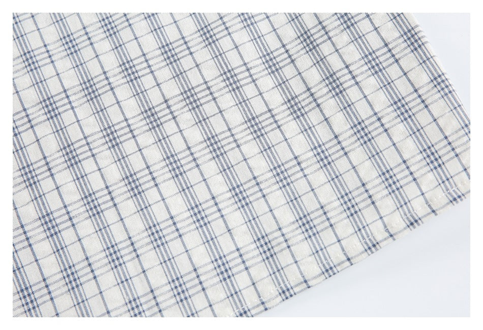 Close-up of the stitched hem on cream fabric with a blue-gray plaid pattern.