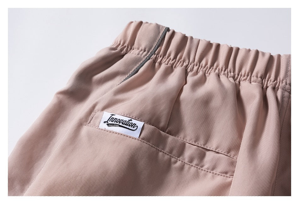 Close-up of dusty rose trousers showing an elastic waistband, pocket, dark zipper, and sewn-in white label.