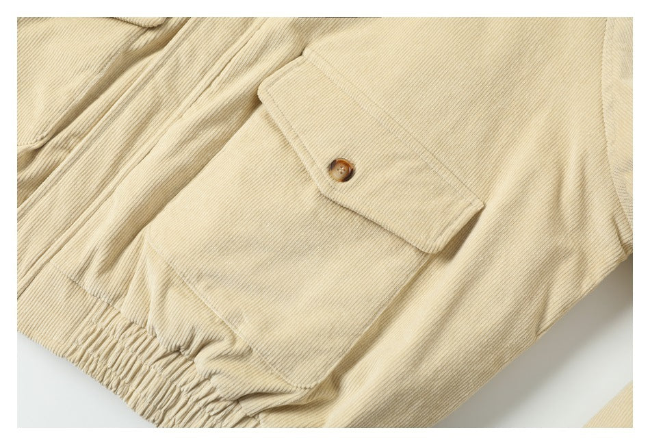Close-up of a cream corduroy jacket showing a flap pocket with a brown button and a gathered hem.