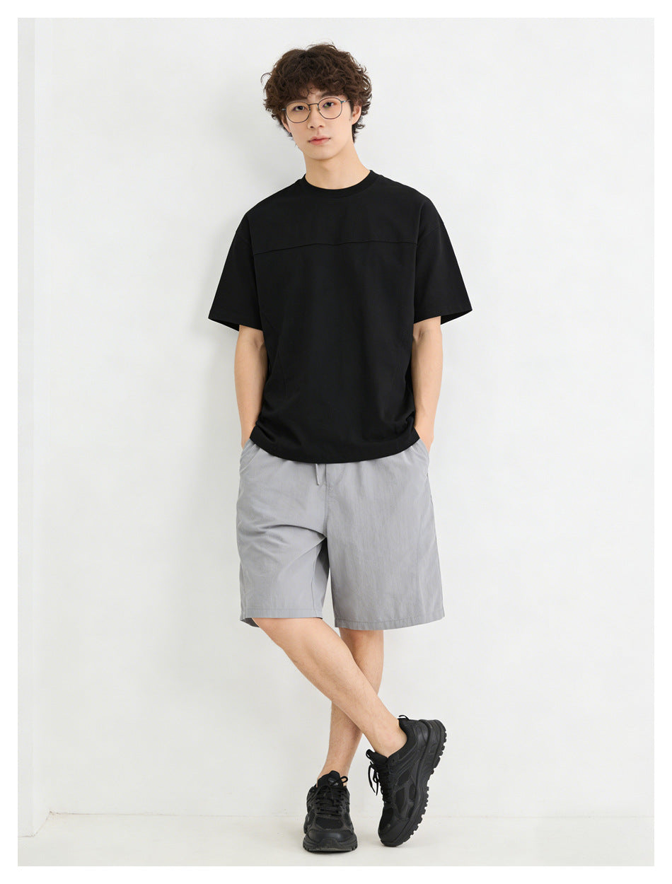 Model wearing a black oversized short-sleeve t-shirt with gray shorts and black sneakers, front view