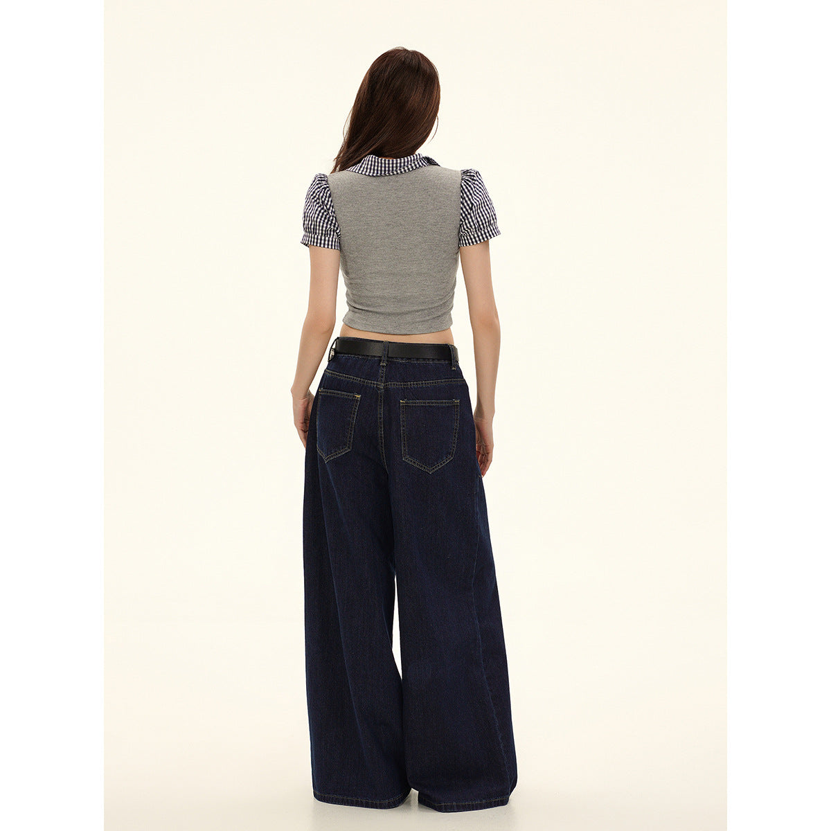 Back view of a model wearing a gray cropped top with gingham collar and sleeves, and dark wide-leg jeans.