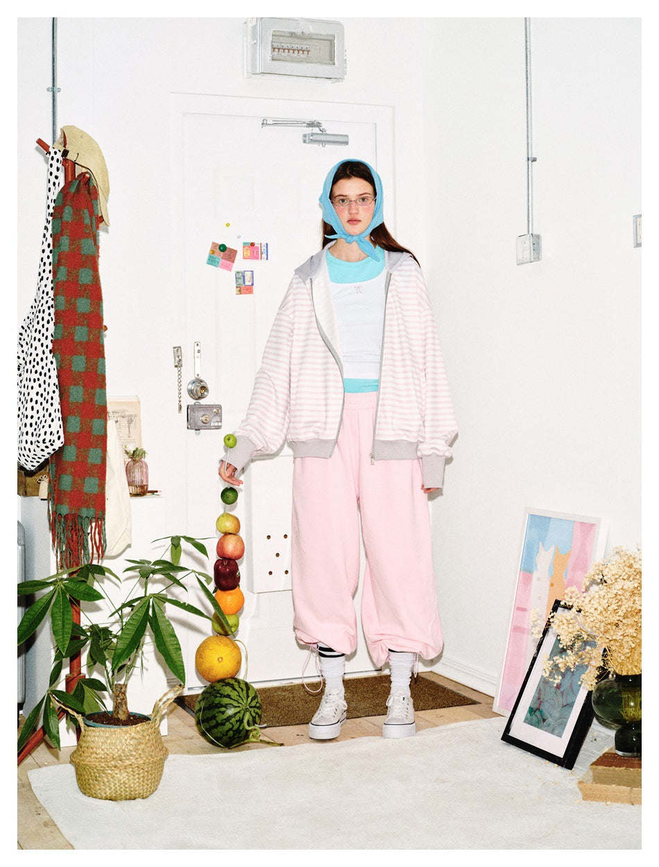 Model standing in an open pink striped hooded jacket with gray trim, white top and pink pants