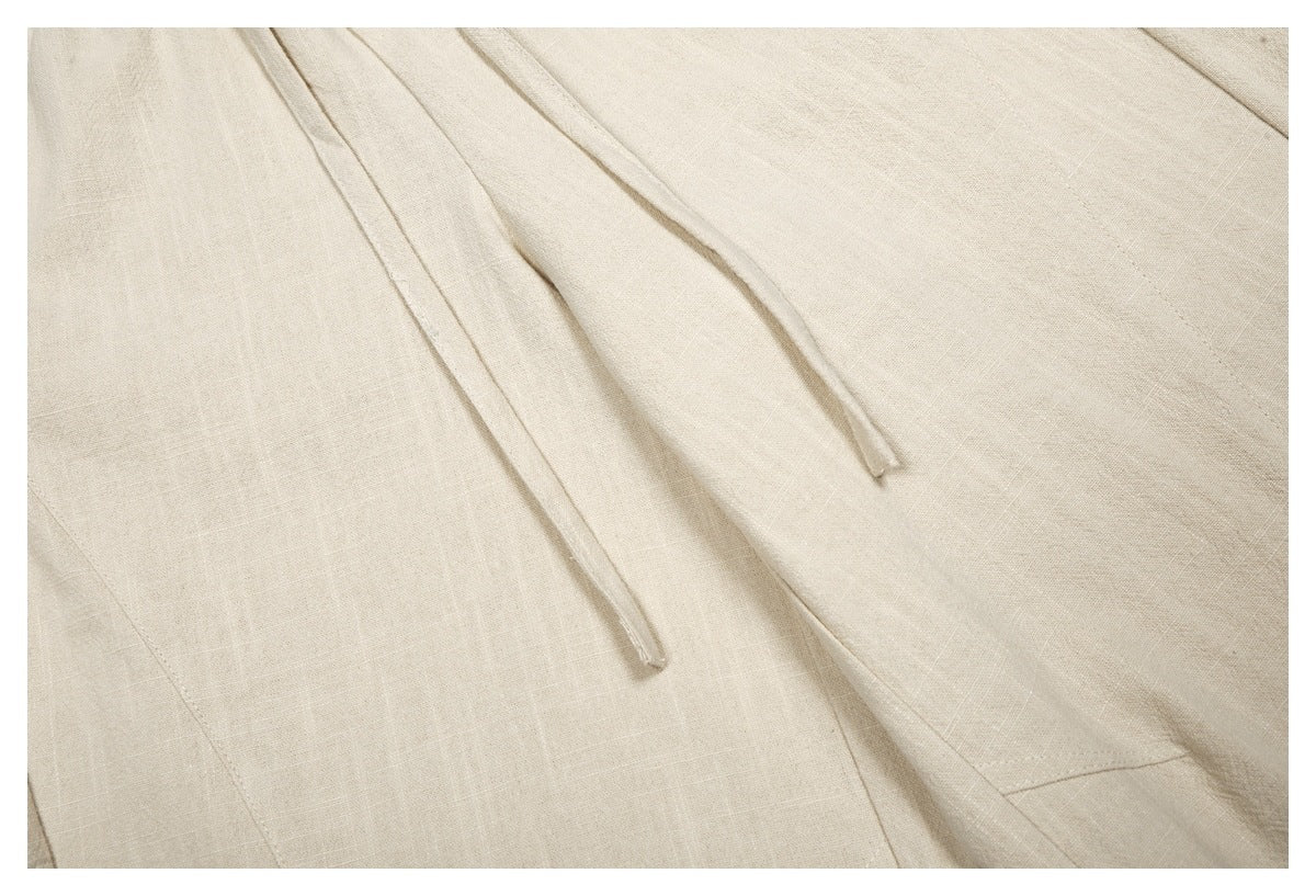 Close-up of beige trouser fabric with two hanging drawstrings and visible stitching.