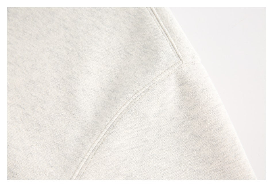 Close-up of curved stitched seams on off-white heathered garment fabric.