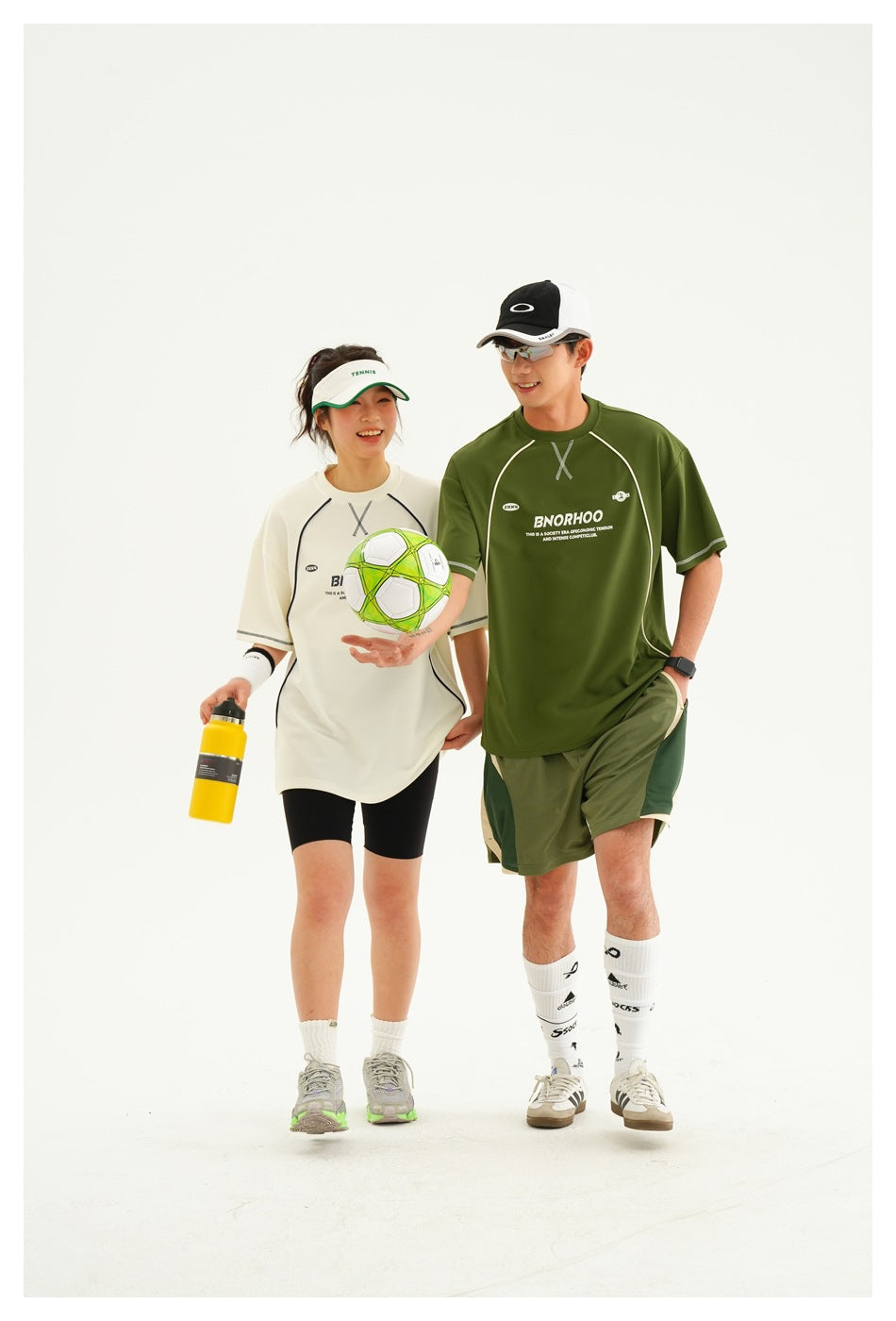 Two models wearing white and olive-green sports T-shirts, with the man in matching color-block shorts.