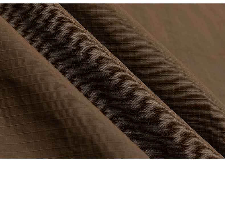 Close-up of brown jacket fabric folded into overlapping layers, showing its fine grid texture.