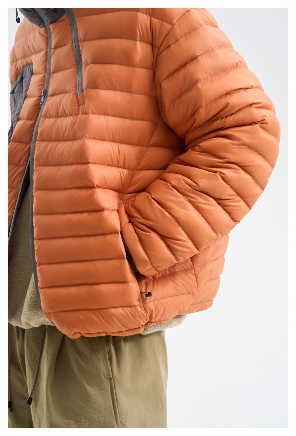 Close-up of the orange puffer jacket's quilted sleeve, cuff, and side pocket on a wearer.