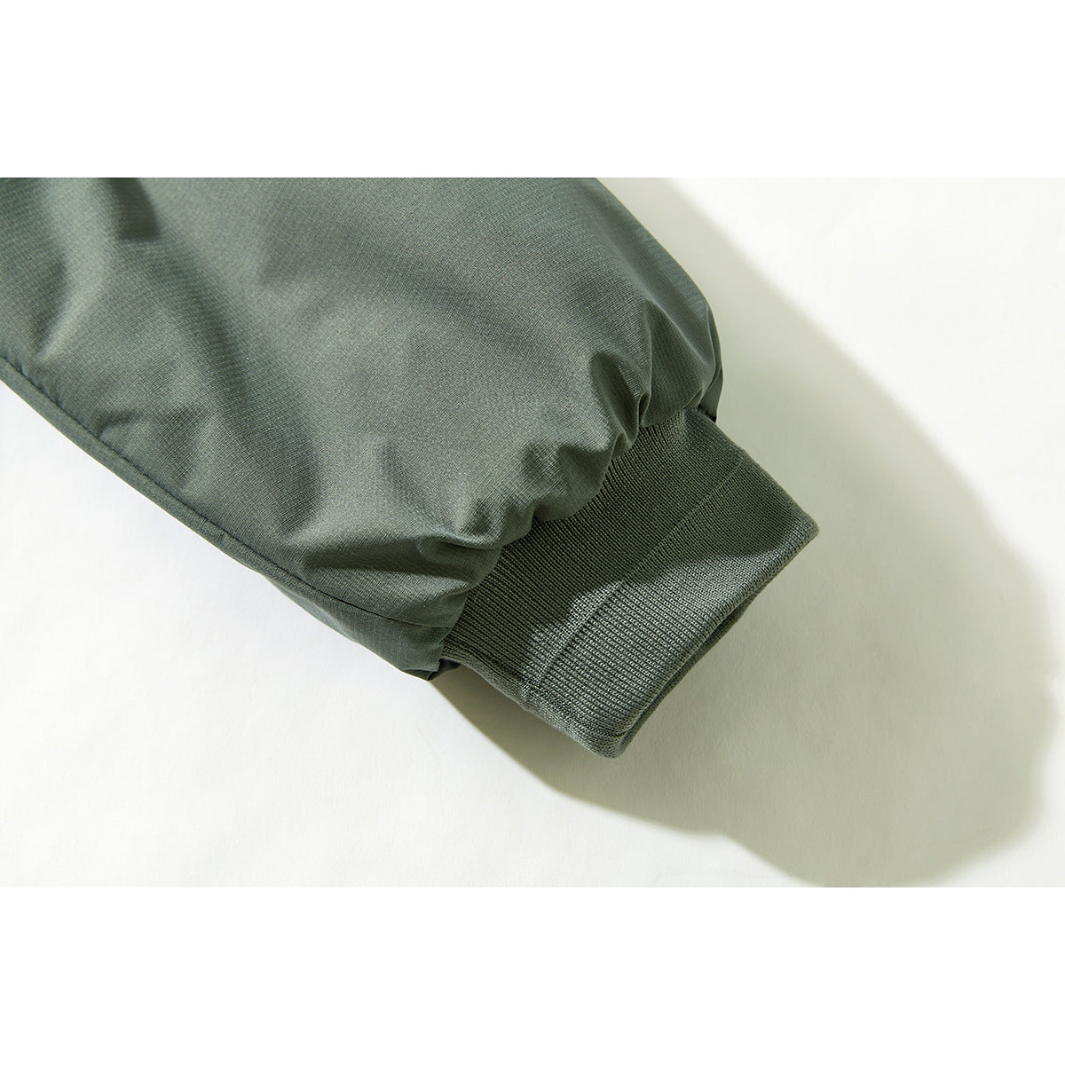 Close-up of a sage green jacket sleeve ending in a ribbed knit cuff.