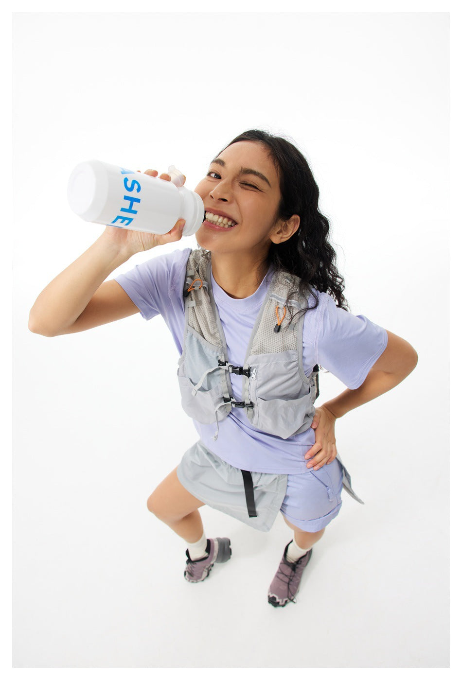 Model in a light purple T-shirt and gray vest drinking from a bottle, high-angle view, T-shirt partly covered