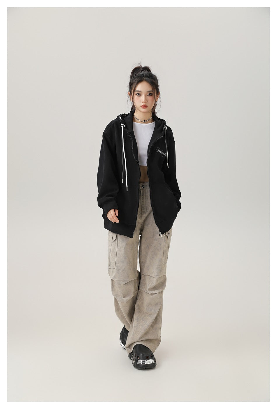 Model wearing an oversized black zip-up hoodie with white drawstrings and a small chest graphic, shown from the front.