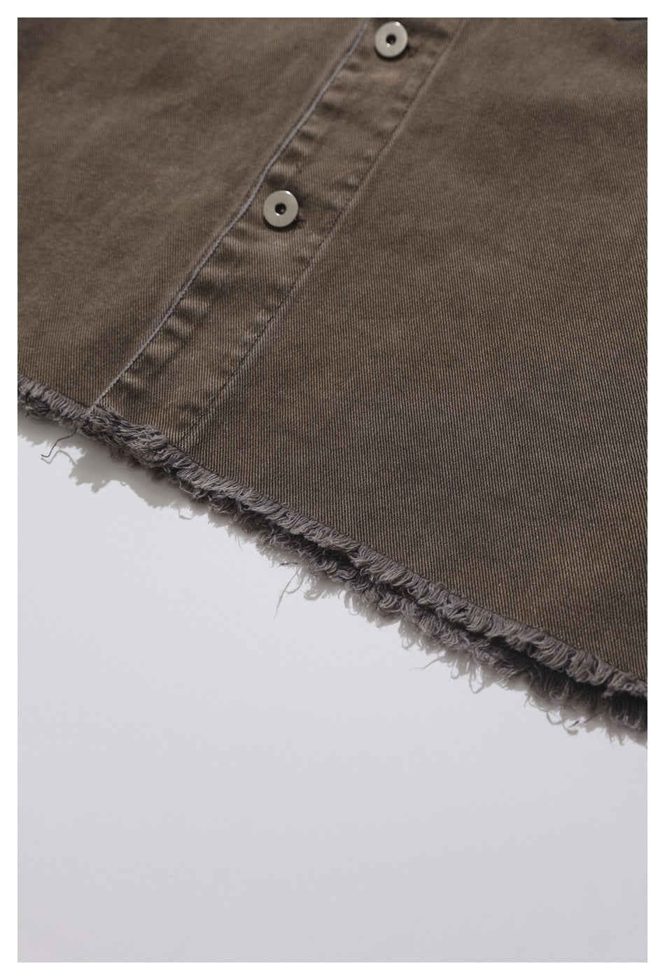 Close-up of a muted brown-gray shirt with metal snaps and a heavily frayed raw hem.