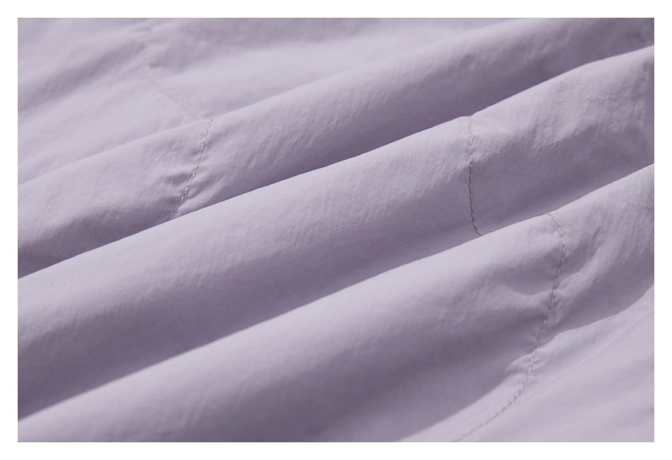 Close-up of pale lavender fabric arranged in folds, showing stitched seams and its surface texture.